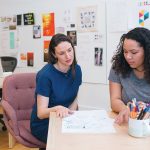 DESIGN TEAM: Sarah Rainwater, center, founder, president and creative director of Studio Rainwater, talks with designer Danikqwa Rambert, right, at the firm’s office in East Providence. Art Director Sarah Verity works in the background.  / COURTESY STUDIO RAINWATER