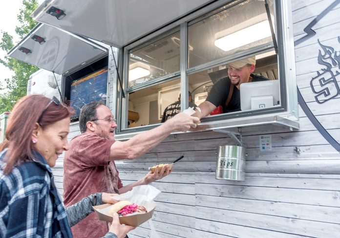 LICENSE TO SELL: Adam Batchelder, right, owns food truck Smoke & Squeal BBQ. He serves Elena and Bob Given, of Mansfield, biscuits, pickled watermelon rind, and mac and cheese. Batchelder says he’ll welcome the chance to get a single statewide license next year. / PBN FILE PHOTO/MICHAEL SALERNO
