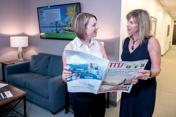 CUSTOMER FOCUS: Ronni Kenoian, left, marketing manager for InsureMyTrip.com, speaks with Martha Manzi, office manager. Kenoian said the company’s focus regarding travel insurance is to serve the customer, rather than make a profit. / PBN PHOTO/MICHAEL SALERNO