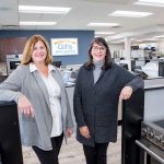 DILIGENT DUO: From left, sisters Gail Almeida Parella and Lisa Almeida Sienkiewicz in their store, Gil’s Appliances in Bristol. The two have worked to modernize the store and make it an integral part of the community.   / PBN PHOTO/KATE WHITNEY LUCEY
