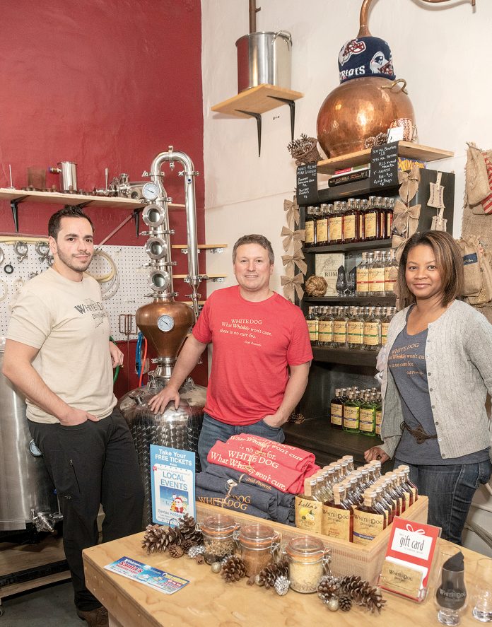 GROWING DISTILLERY: White Dog Distilling, incorporated as CAVE LLC, was founded in 2016 by Carlo Catucci, center, and his wife, Alecia, right, who partnered with longtime friends Eric Sylvestre, left, and Vin Greene, not pictured. Their micro-distillery and tasting room opened last April in a historic mill space in Pawtucket and will be moving to a larger retail location within the mill.  / PBN PHOTO/MICHAEL SALERNO