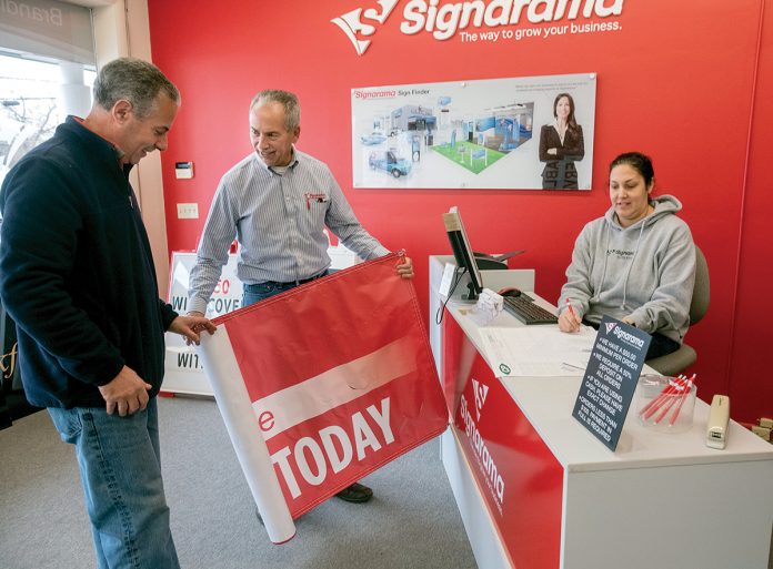 REWARDING WORK: Joe Lomastro, center, franchise owner of Signarama on Post Road in North Kingstown, with Tom Iacobucci, owner of Sears Hometown Store, and Lauren DeAquair, graphic designer.  / PBN PHOTO/MICHAEL SALERNO