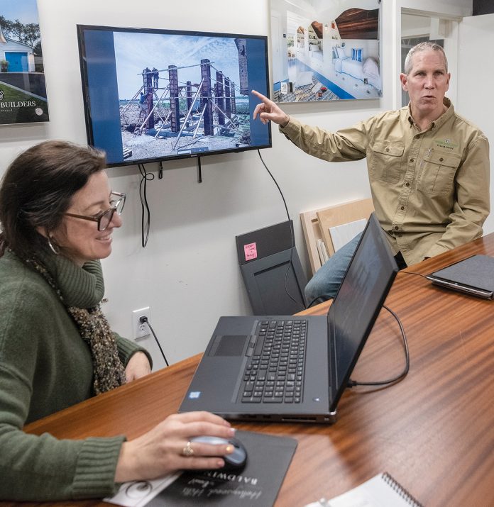 WEATHER-RESISTANT: Jeff Sweenor, owner of Sweenor Builders in South Kingstown, points to the house that architectural designer Lori Foley has on screen that is located in South Kingstown and uses helical piers that screw down to bedrock and breakaway lower walls that let the water go right through. / PBN PHOTO/MICHAEL SALERNO