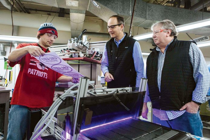 BY DESIGN: Printer Tom Willis, left, shows freshly printed graphics to NFI President Renaud Megard, center, and Manufacturing Director Mark Smith.  / PBN PHOTO/RUPERT WHITELEY