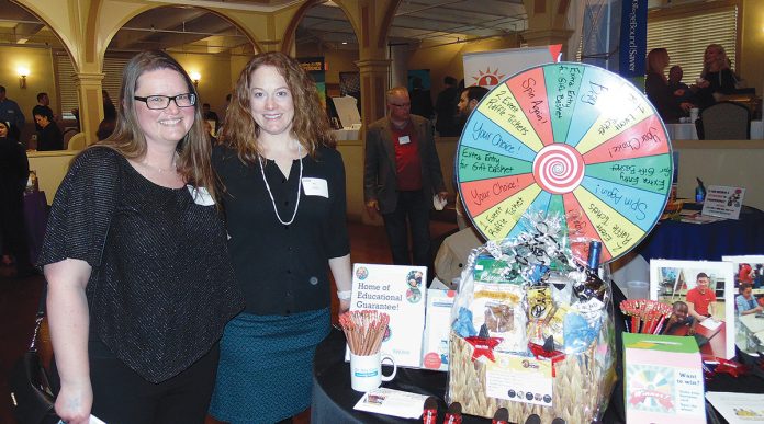 AFTER HOURS: Dr. Day Care representatives Rebecca Compton, left, and Amy Vogel stand near their display, which includes a game wheel, during last year’s Statewide Business After Hours networking event. This year’s event will be held on March 26 at the Rhodes on the Pawtuxet in Cranston.    / COURTESY NORTHERN RHODE ISLAND CHAMBER OF COMMERCE