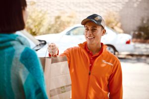 HOME DELIVERY: A Panera Bread employee delivers a meal order to a customer. Panera Bread and local franchisee Howley Bread Group have built their own delivery infrastructure, enabling the fast-casual chain to retain customer loyalty and customer data, rather than utilizing a food-delivery app.  / COURTESY HOWLEY BREAD GROUP