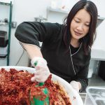 MIX IT UP: Chi Foods CEO Minnie Luong stirs the ingredients for a fresh batch of kimchi in the company’s kitchen.  / PBN PHOTO/ RUPERT WHITELEY