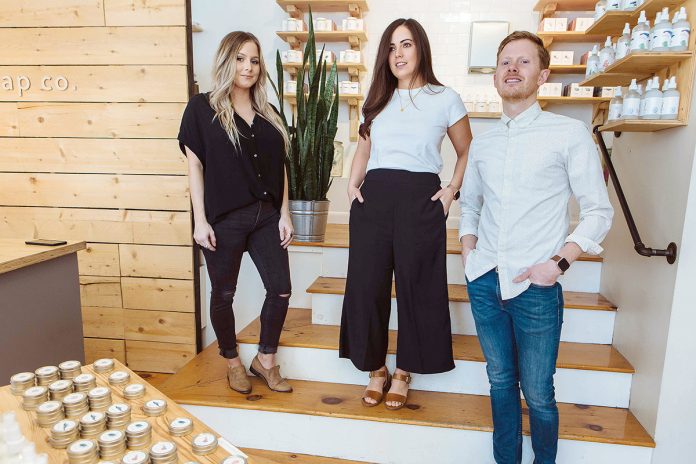 HOMEMADE BEGINNINGS: From left, store manager Brandi White with co-owners Steph and Jake Kopper at Shore Soap in Newport. The Koppers opened the shop at the suggestion of friends and family who were impressed with the couple’s homemade 12-bar batches of soap, which began as a hobby.  / PBN PHOTO/RUPERT WHITELEY