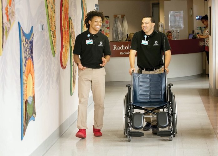 SMOOTH RIDE: Elijah Matthews, left, and Xavier Rivera work in central transport at Rhode Island Hospital in 2018. The job, often filled in the summer by interns, involves moving patients and equipment.  / COURTESY LIFESPAN CORP.