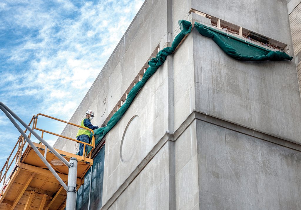 SKY HIGH: Rehab mason Mike DeQuattro chisels the deteriorated limestone strip at the top of the fascia of the library’s Empire Street wing. DeQuattro works for Boston-based The Water Proofing Co.  / PBN PHOTO/MICHAEL SALERNO