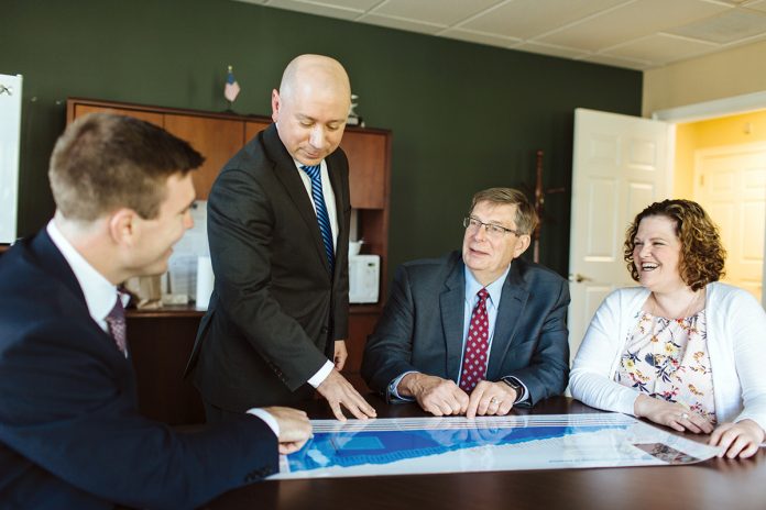 HUDDLE UP: Edward Jones financial adviser Eric Milhoua, standing, talks numbers with, from left, advisers Tom Gardiner and Frank Wallington, and office administrator Ashley Bickford, in Westerly.  / PBN PHOTO/RUPERT WHITELEY