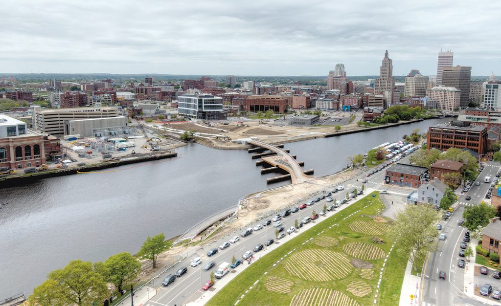 DEVELOPABLE LAND: Shown is an aerial shot of developable land in the Interstate 195 district of Providence. The Wexford Innovation Center is at center in the background and the Providence Pedestrian Bridge is in the foreground extending over the Providence River. The two land areas connecting the bridge will be developed into public parks.  / PBN PHOTO/ARTISTIC IMAGES