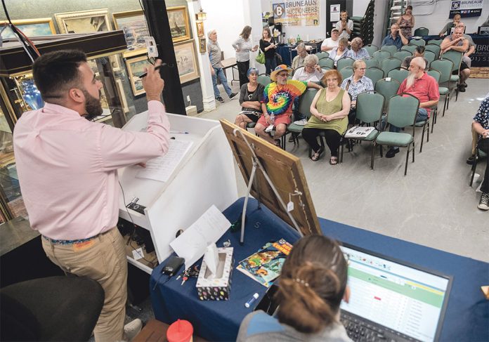 ONLINE PRESENCE: Auctioneer Travis Landry takes bids from the crowd, as well as online, during an auction at the Bruneau & Co. Auctioneers gallery in Cranston. Gallery owner and President Kevin Bruneau said most of their auctions feature online bidders from around the world competing with live audiences, pulling in up to 10,000 additional bidders who check in on auctions periodically. / PBN PHOTO/MICHAEL SALERNO