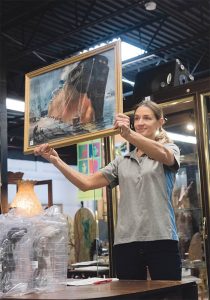 GOING ONCE: Gallery assistant Heidi Kirchner holds up “Industrial Tanker,” a painting by Spencer Crooks, for bids during an auction at Bruneau & Co. Auctioneers in Cranston. / PBN PHOTO/MICHAEL SALERNO