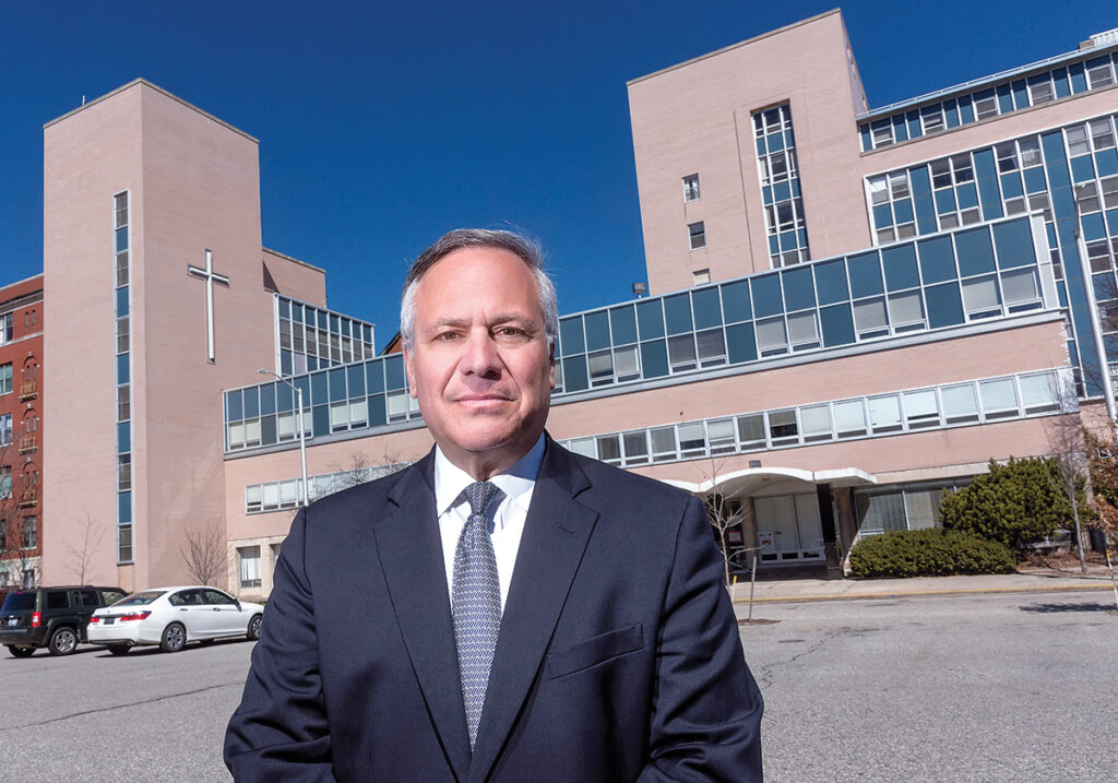 DISPUTE: Former Providence Mayor Joseph A. Paolino Jr. stands in front of the former St. Joseph’s Hospital. Paolino is listed as the registered agent of both 21 Peace Street LLC and Urban Land Development Co. LLC, which are the corporate owners of the former hospital. A disagreement over whether a tax-stabilization agreement can be lifted with a property sale is at the center of a dispute between Providence and the owners.  / PBN FILE PHOTO/MICHAEL SALERNO
