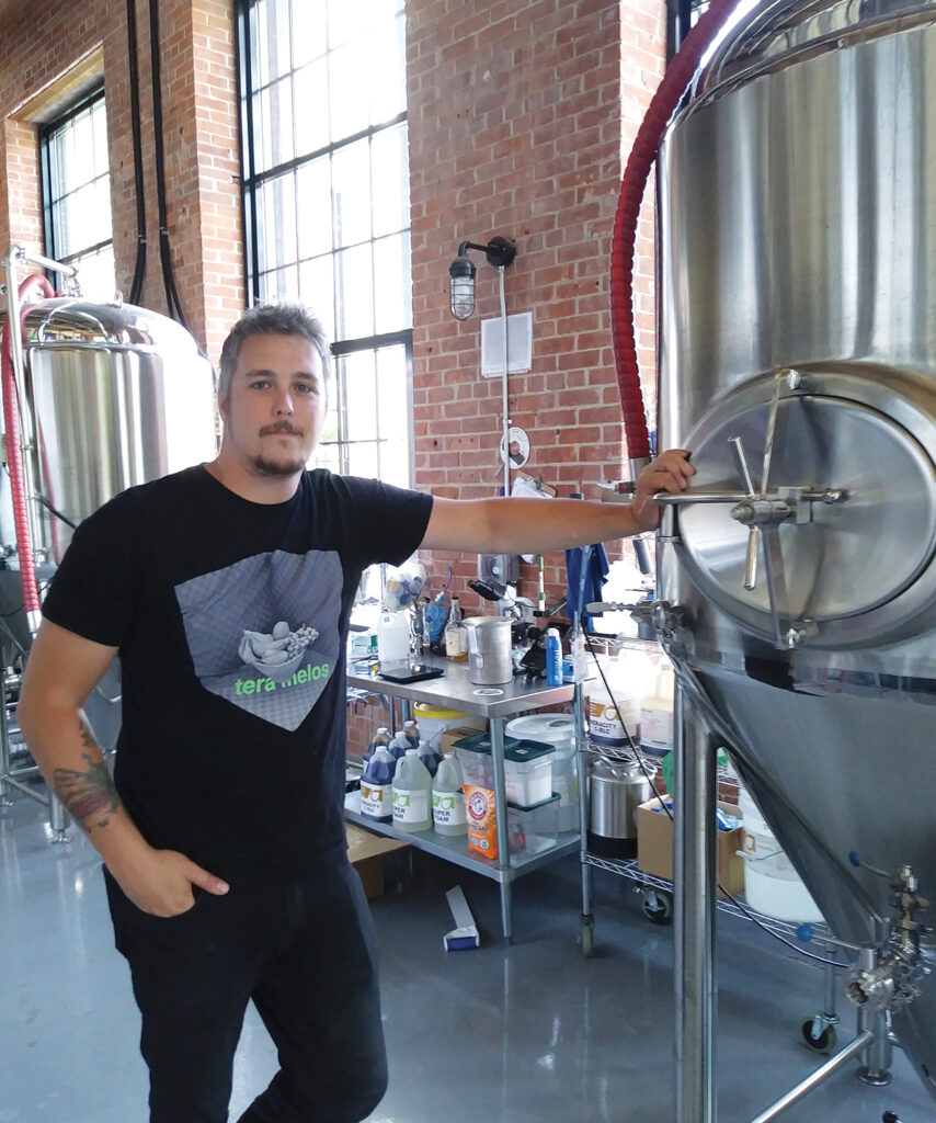 ECLECTIC BREWS: Head brewer Justin Tisdale stands in front of one of the tanks at Apponaug Brewing. There are eight to 10 craft brews on tap daily at the brewpub in the former Pontiac Mills building in Warwick.   / PBN PHOTO/BRUCE NEWBURY