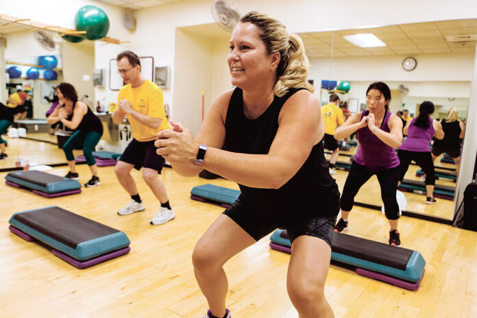 IN STEP: Kristen Boudreau, center, an International Game Technology supply chain analyst, works up a sweat in a step class at the corporate fitness center in West Greenwich. With her, from left, are co-workers Tracie Angelo, Predrag Stojkov and Yanna Tow.  / PBN PHOTO/RUPERT WHITELEY