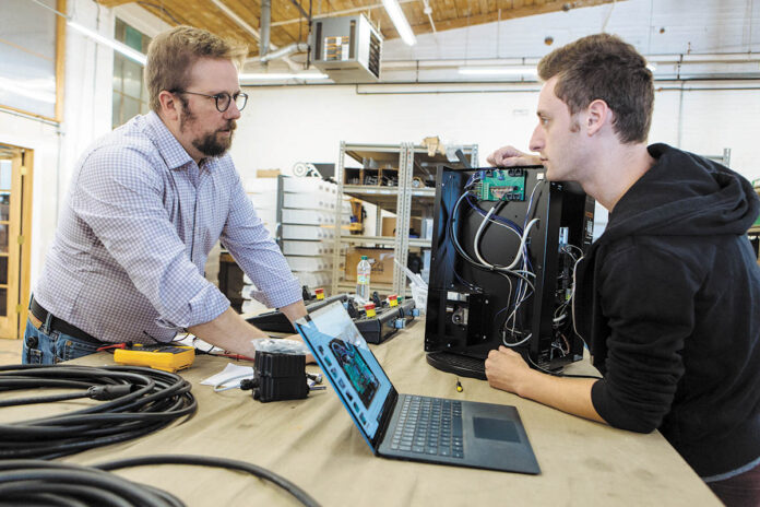 SETTING THE STAGE: Gareth Conner, left, founder and president of Creative Conners Inc., talks with automation technician Josh Stoller about a product Stoller is working on. It’s a Spotline Practical hoist used in theatrical shows.     PBN PHOTO/RUPERT WHITELEY