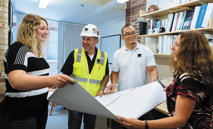 ACCORDING TO PLAN: From left, Assistant Project Manager Taylor Huntly, Superintendent Marty Mendonca, Senior Project Manager Chi Yik and Manager of Project Administration Sharon Barbary unfurl blueprints in the Providence office of Shawmut Design and Construction. PBN PHOTO/RUPERT WHITELEY