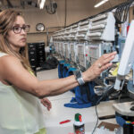 FINISHED ORDER: Machine operator Claudia Herrera completes an order at ParsonsKellogg in East Providence. The company prints and embroiders company logos on products for promotional purposes.  / PBN PHOTO/MICHAEL SALERNO