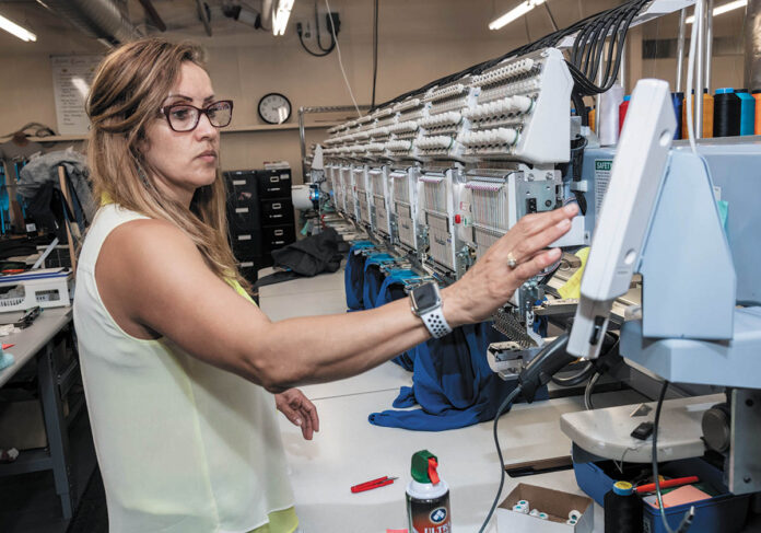 FINISHED ORDER: Machine operator Claudia Herrera completes an order at ParsonsKellogg in East Providence. The company prints and embroiders company logos on products for promotional purposes.  / PBN PHOTO/MICHAEL SALERNO
