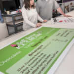 FINE PRINT: Karen Martins, left, franchise owner of FastSigns in Seekonk, inspects some placards with production/project installation manager Eric Dallaire. / PBN PHOTO/MICHAEL SALERNO