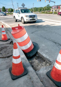 IN NEED OF REPAIR: An R.I. Department of Transportation vehicle avoids road cones and a traffic barrel surrounding a deep hole on New London Avenue in Cranston. A $20 million bond passed in 2016 is funding current roadwork, along with other highway department needs, in the city.   / PBN PHOTO/MICHAEL SALERNO