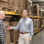 PAPER PUSHERS: David Spencer, right, CEO of Atlantic Paper & Supply, talks with sales representative Sean Borek. Spencer runs the company with his wife, Lisa, whose grandfather started the business in the 1940s. / PBN PHOTO/MICHAEL SALERNO